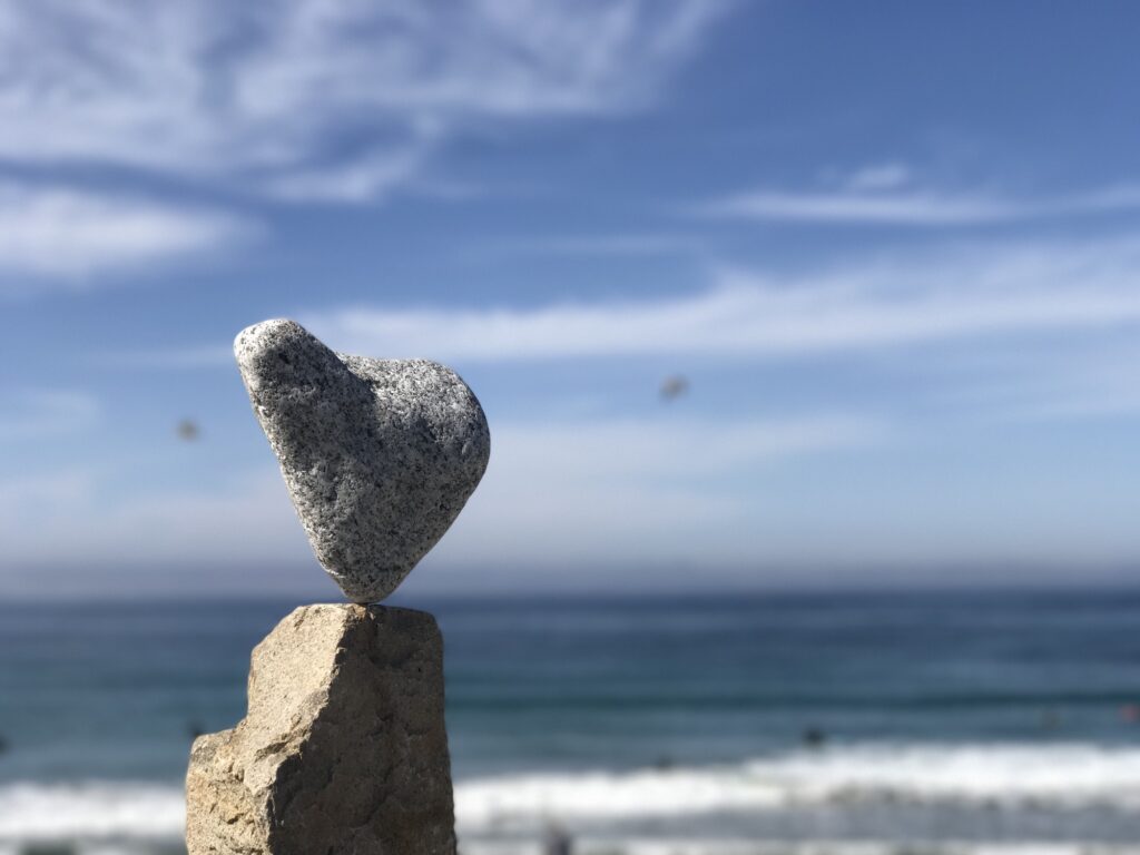 A rock in the shape of a heart representing love balances at the beach or ocean.